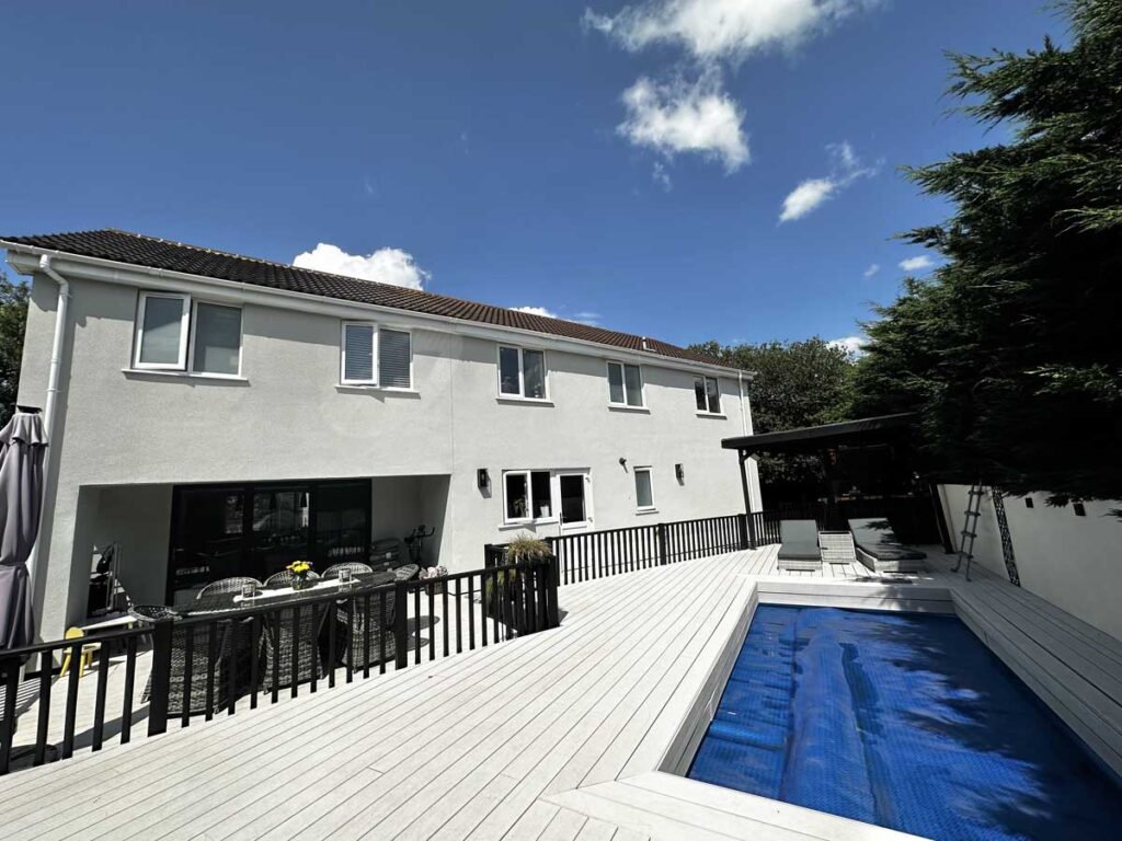 Large rendered home with rear extension and outdoor decking area overlooking garden